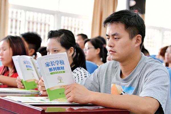 A father focusing hard on reading a parenting book while attending a parenting class in Anhui. 