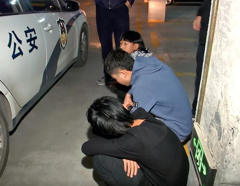 Three young Chinese men are lined up against the wall after being detained by police and prepare to be taken to a local police station.