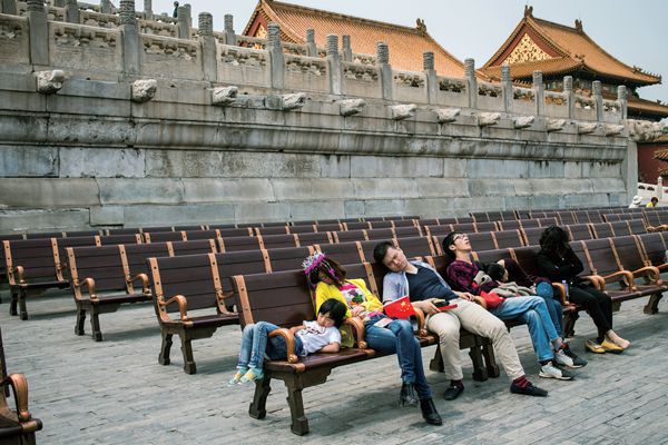 A Chinese family napping on some bench seats outside a palace entrance. 
