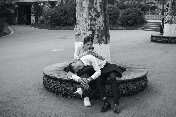 A Chines man taking a nap on a woman's lap as she takes browses on her phone.