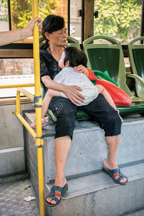A young child takes a siesta on her grandmother&#x27;s lap while riding a bus. 