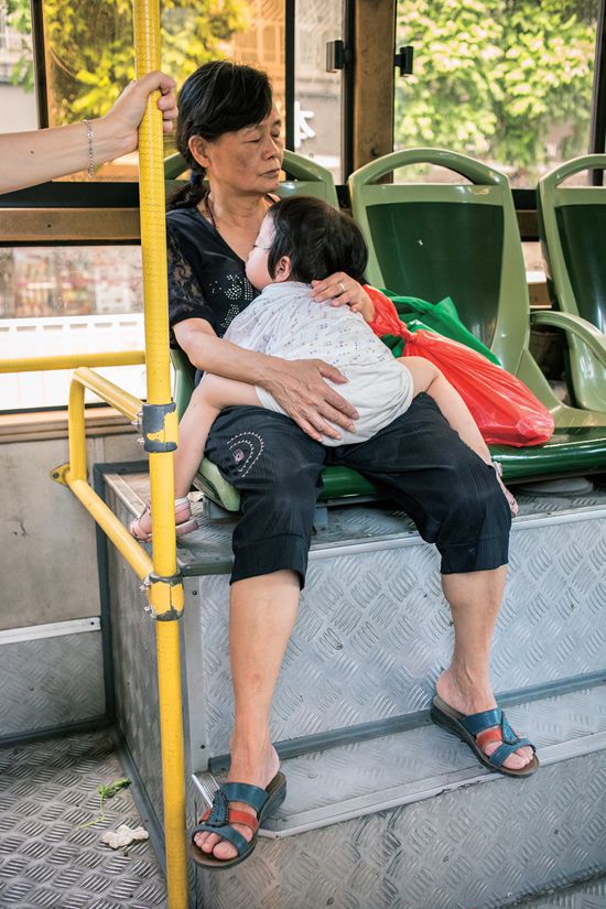 A young child takes a siesta on her grandmother's lap while riding a bus.