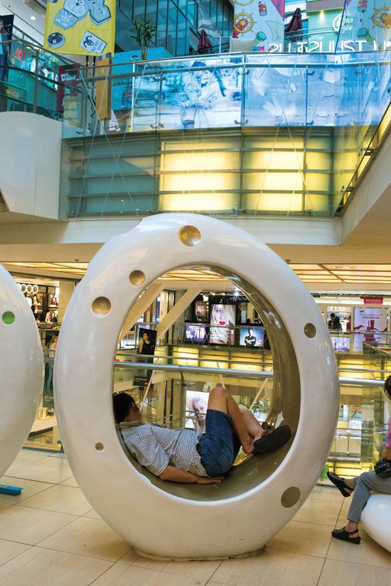 A Chinese man taking an afternoon nap in an egg-shaped dome at a mall.