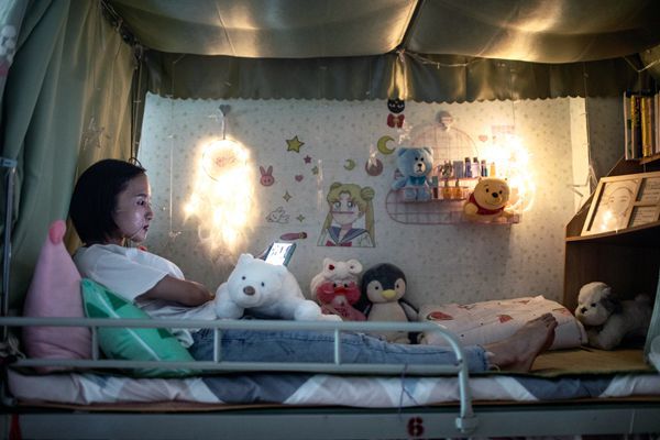 A young Chinese factory worker lays on her bunkbed as she applies a face mask at night.
