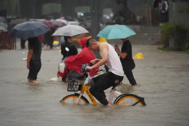 A Zhengzhou resident attempts to ride his yellow ebike through the floodwater in Zhengzhou (VCG)