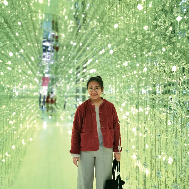 Peng Yujiao, a feminist standing in a room of brightly lit green lights in the background..