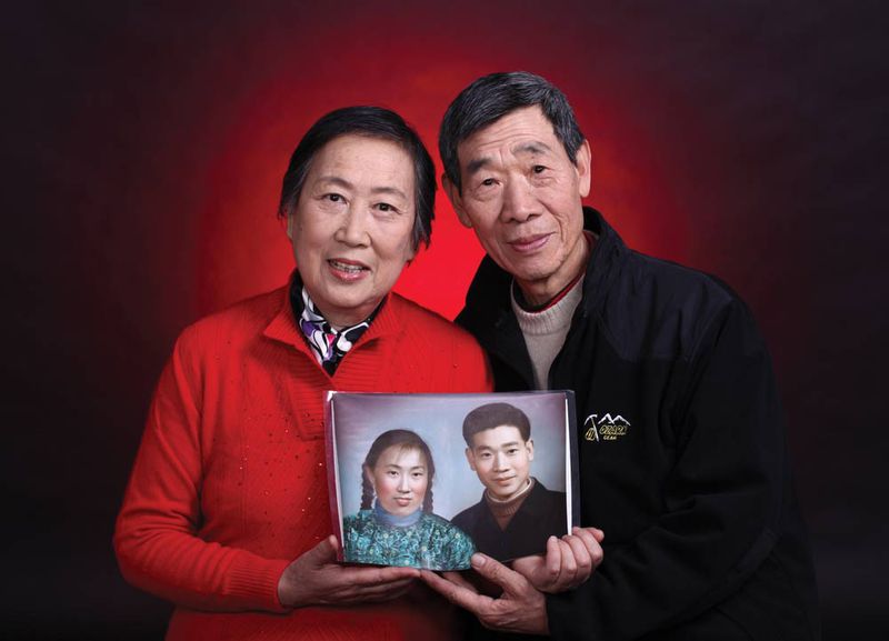 A couple's golden wedding anniversary photo taken at China Photo Studio in which they hold their original photo taken at the same studio