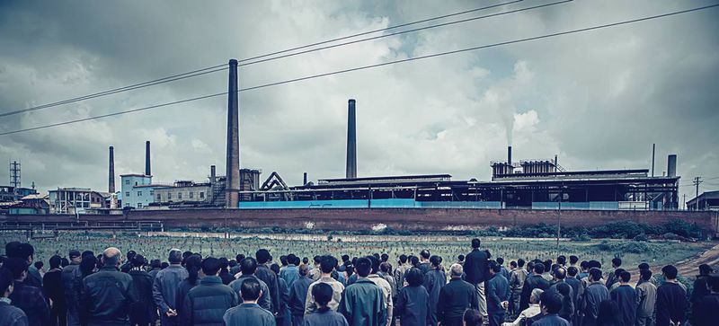 A crowd gathers outside the factory gates, where a body is discovered in the film's opening scenes